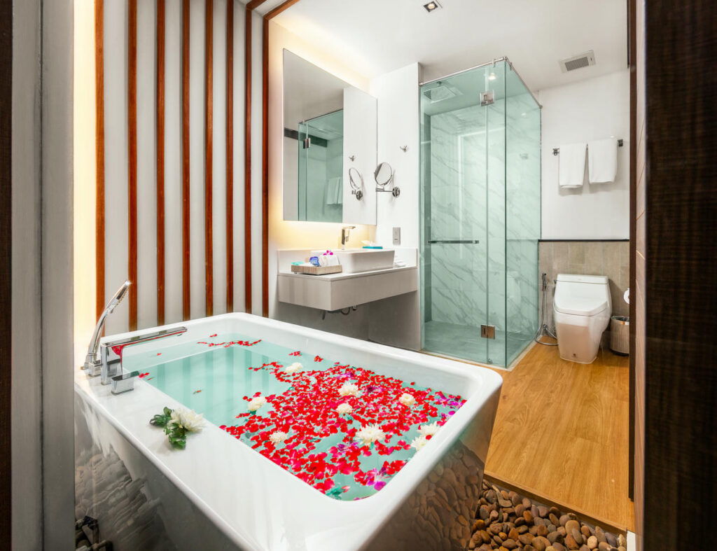 Bathroom in the Deluxe Twin Room with bathtub decorated with floating flowers, closet, sink, and separate shower area