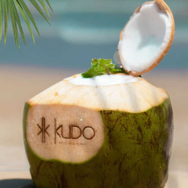 Coconut drink with KUDO Hotel and Beach Club logo by the beach
