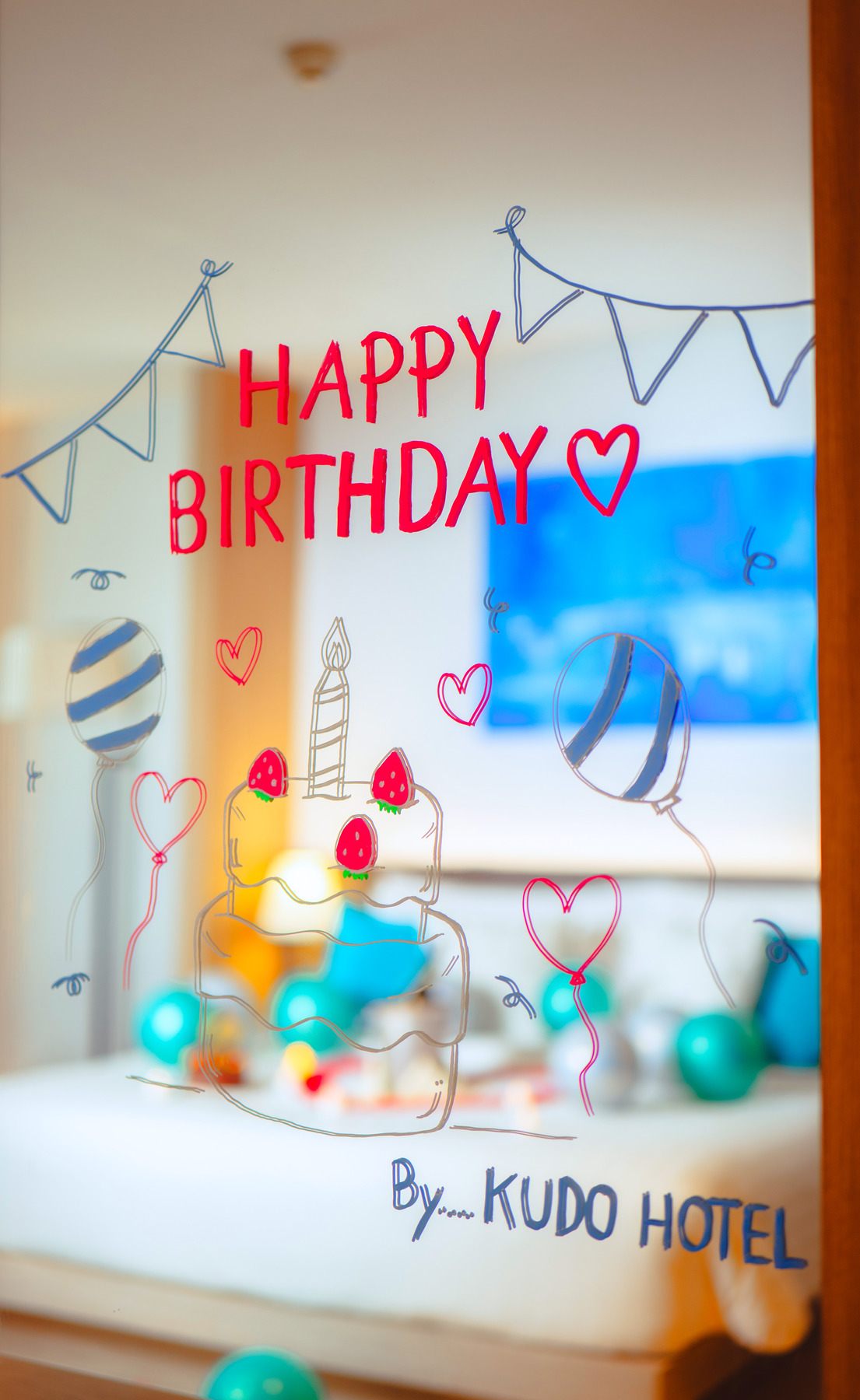 Birthday-themed mirror decoration with balloons, cake illustration, and “Happy Birthday” text, styled by Kudo Hotel for special occasions.